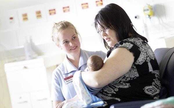 Midwifery student on placement talking to patient with baby