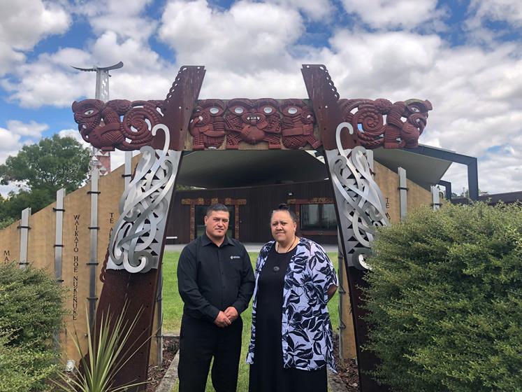 Dion Ormsby and Karen Bishop-Puhi stand in front of the tomokanga at Te Kōpū Mānia o Kirikiriroa Marae at Wintec