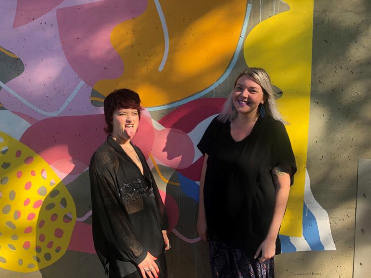 Lauren Mann and Kat Waswo pose in front of a mural.