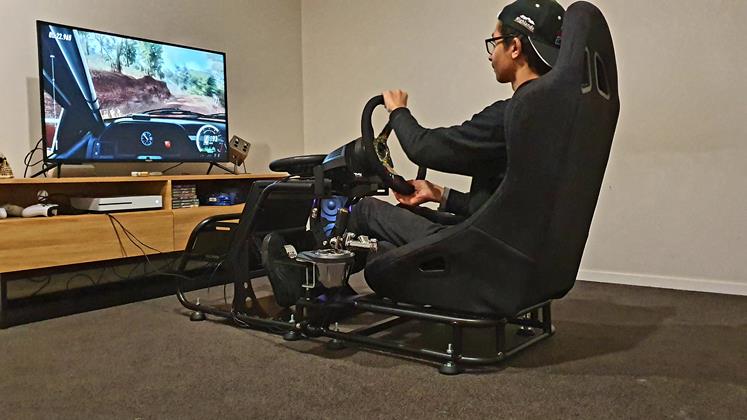 Man sits in race simulator rig playing a racing video game. 