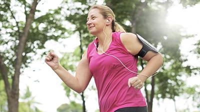 Female runner jogging through forest listening to music