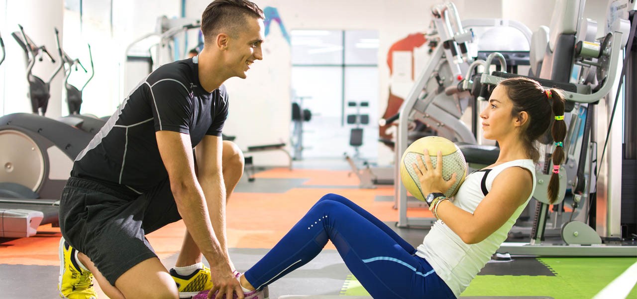 Personal trainer helping client undertake sit-ups in a gym