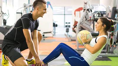 Personal trainer helping client undertake sit-ups in a gym